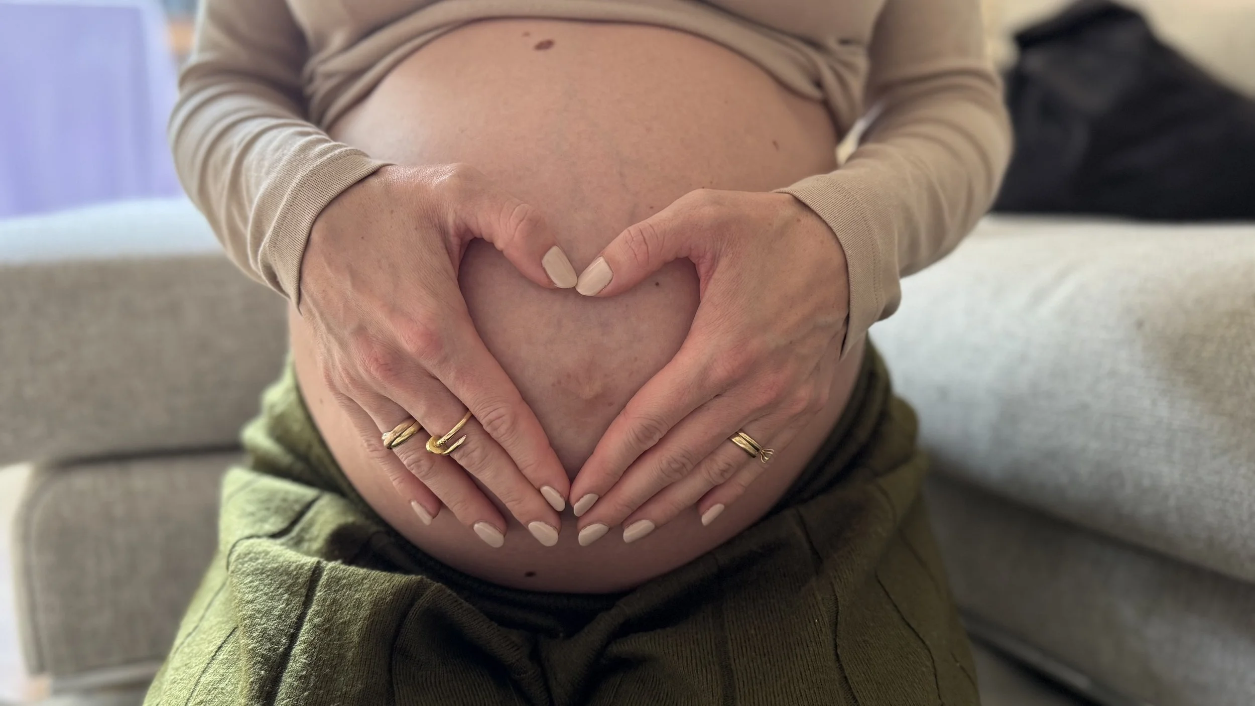 A pregnant woman showing her bare belly, making a heart shape with her hands.