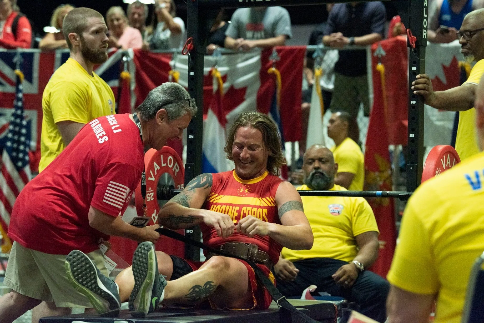 Coach LJ assisting an adaptive athlete during a bench press event at a strength competition.