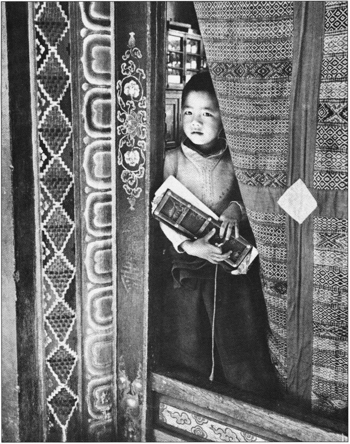A young boy standing behind a door, holding a book, looking outside with a curious expression, in a setting with patterned curtains and ornate wooden furniture.