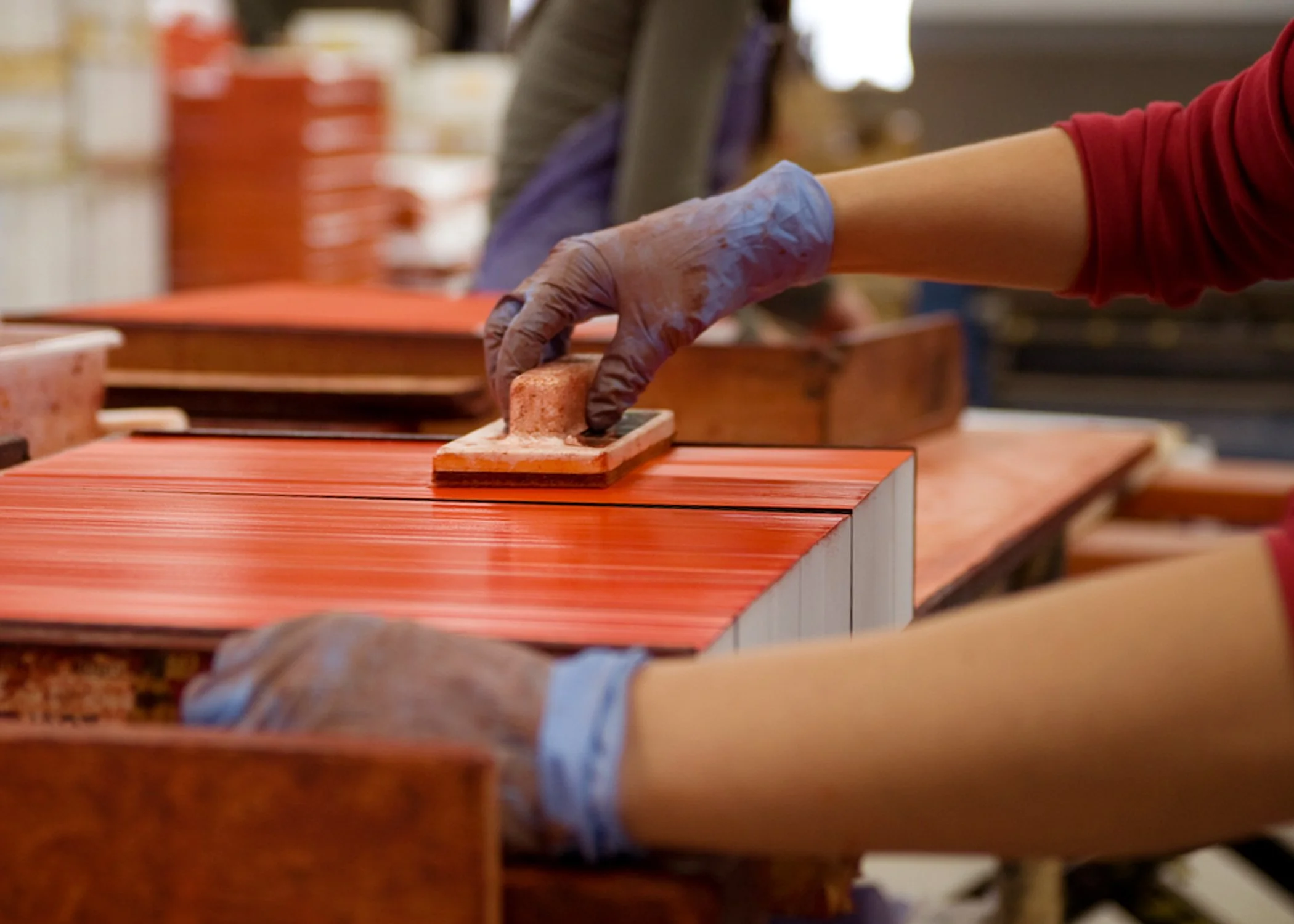 Close up of hands of a volunteer preparing books in a bindery. They are wearing gloves and using a tool to apply special dye to the edges of traditional style texts. 