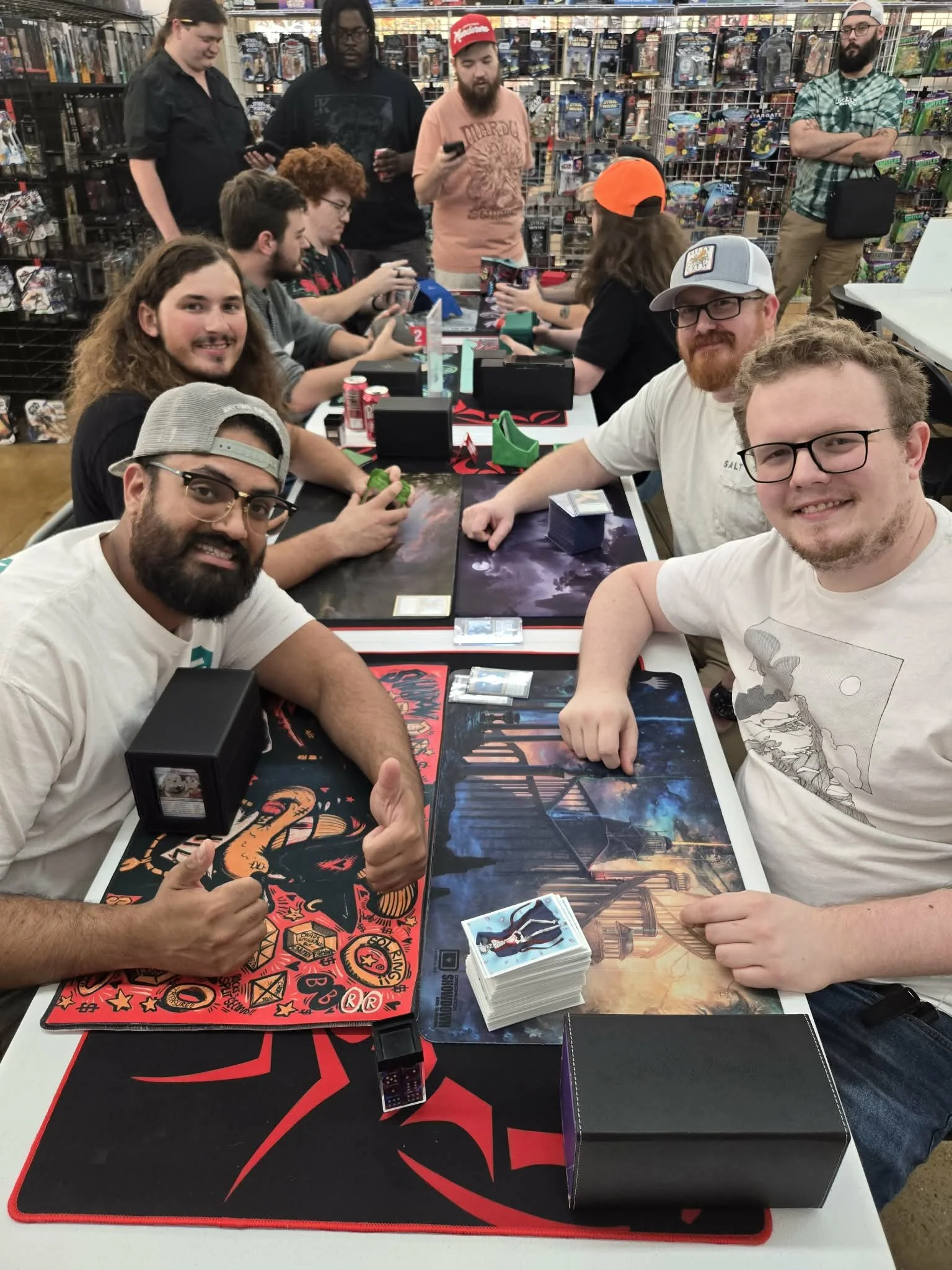 A group of people gathered around a table playing a trading card game in a store, with some people standing in the background.