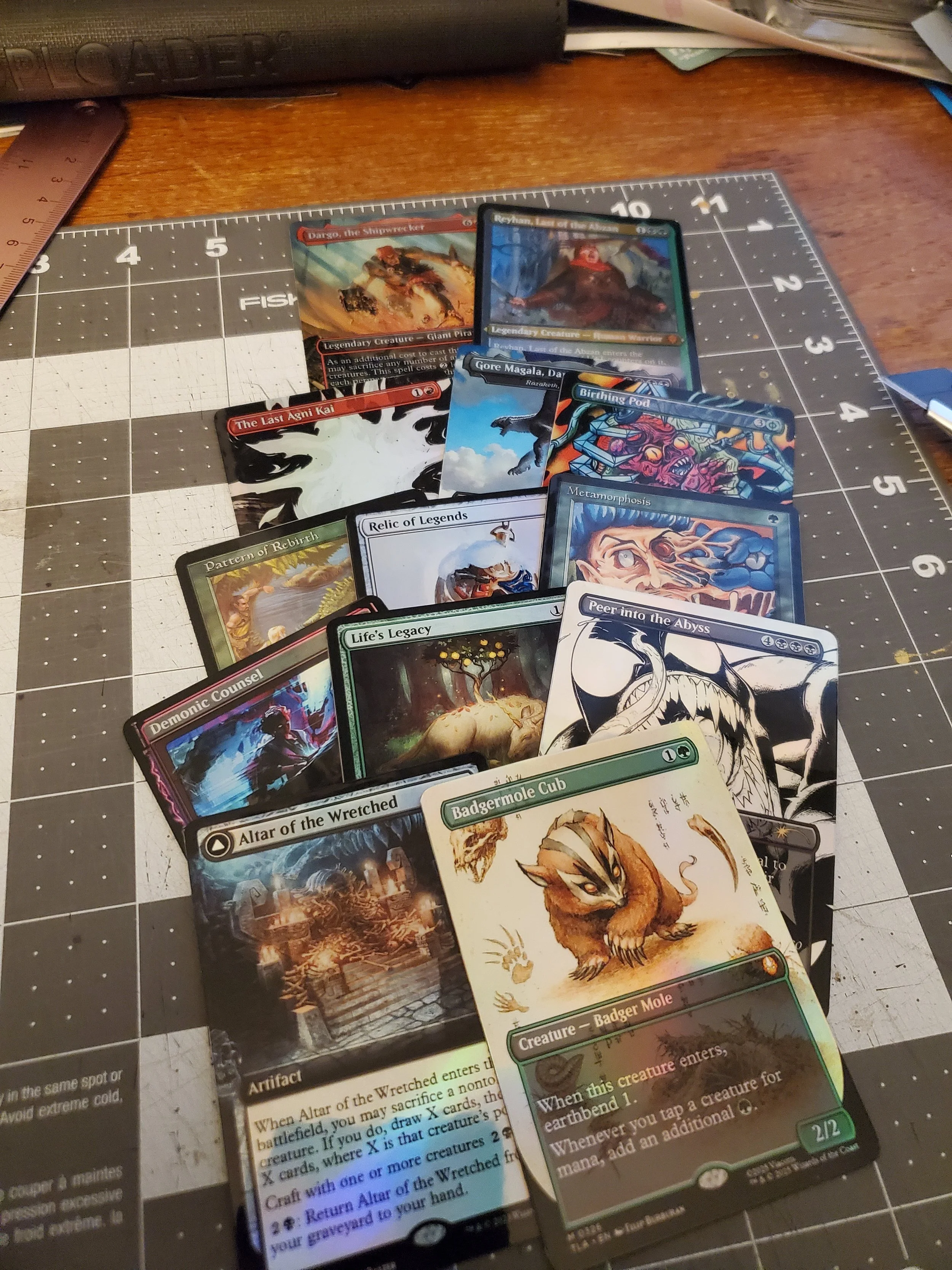 A collection of Magic: The Gathering cards laid out on a craft mat, including cards like Altar of the Wretched, Badgermole Cub, Peer into the Abyss, and others.