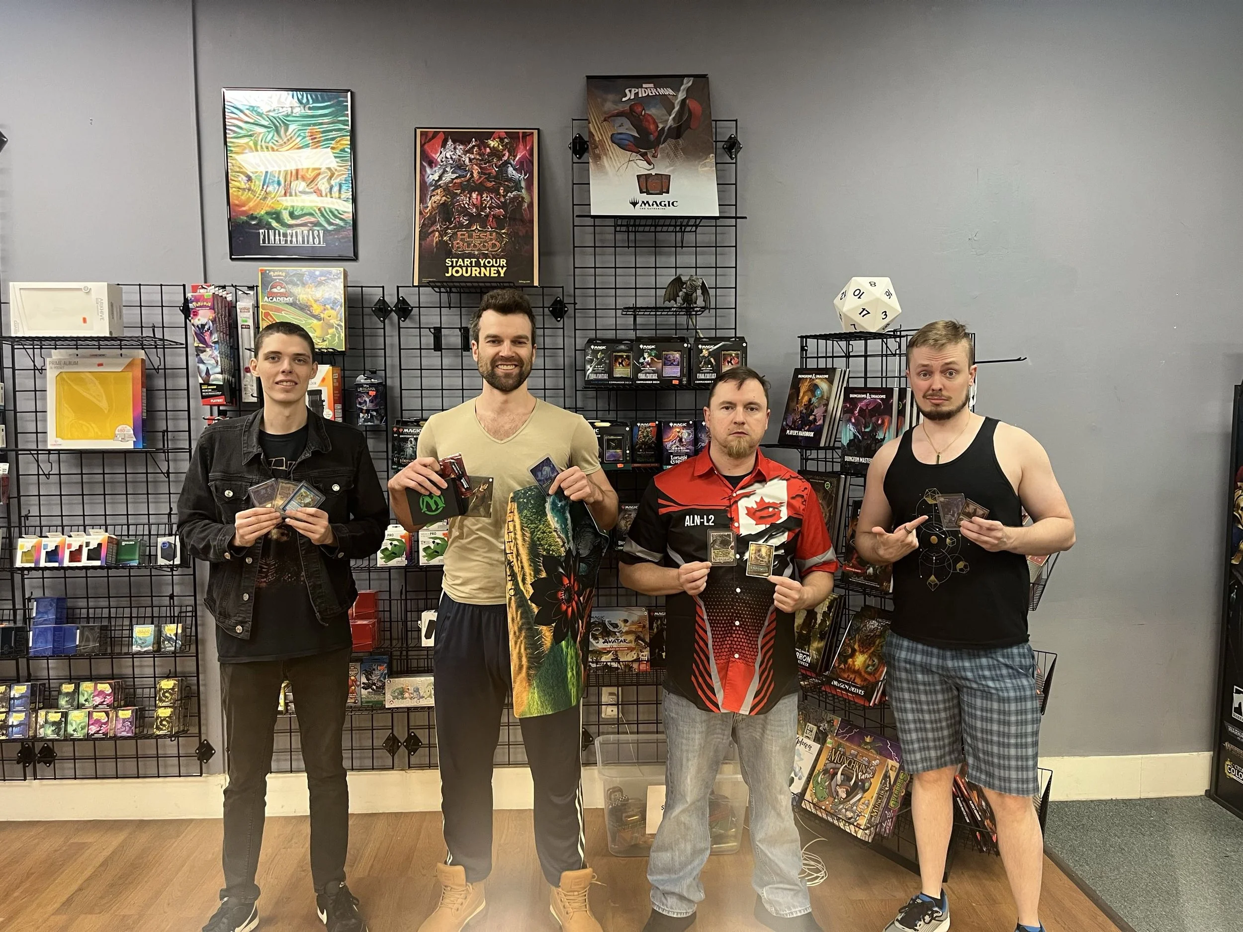Four men standing in front of a game shop wall filled with board games and posters, holding trading cards and gaming accessories.