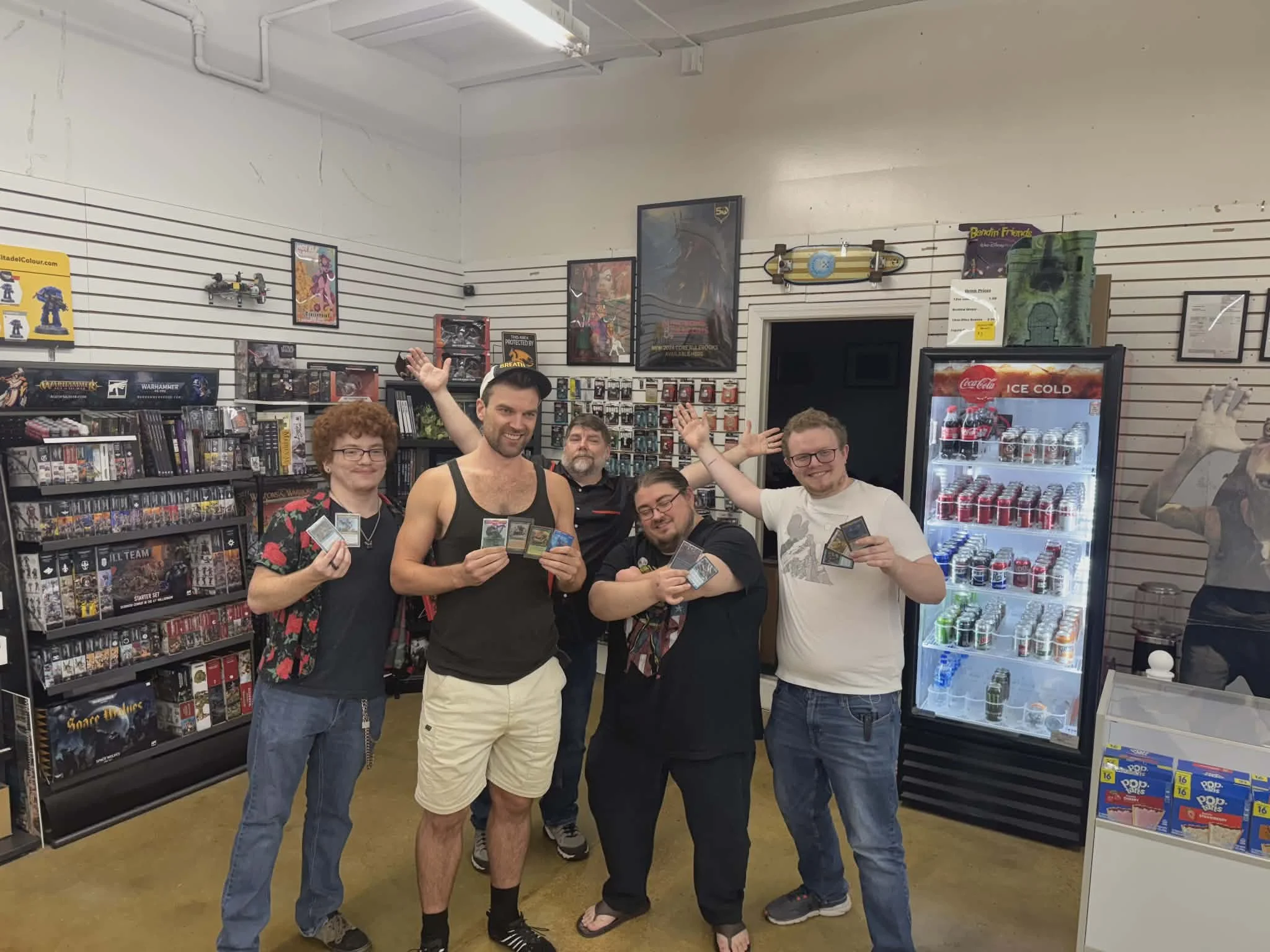 Five friends in a game store holding trading cards, smiling and celebrating.