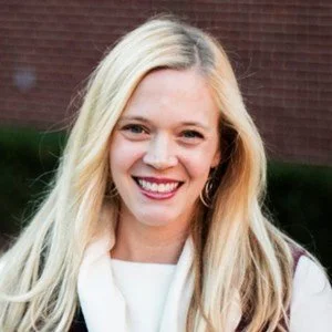 Headshot of a woman with blonde hair smiling into the camera with a brick background.