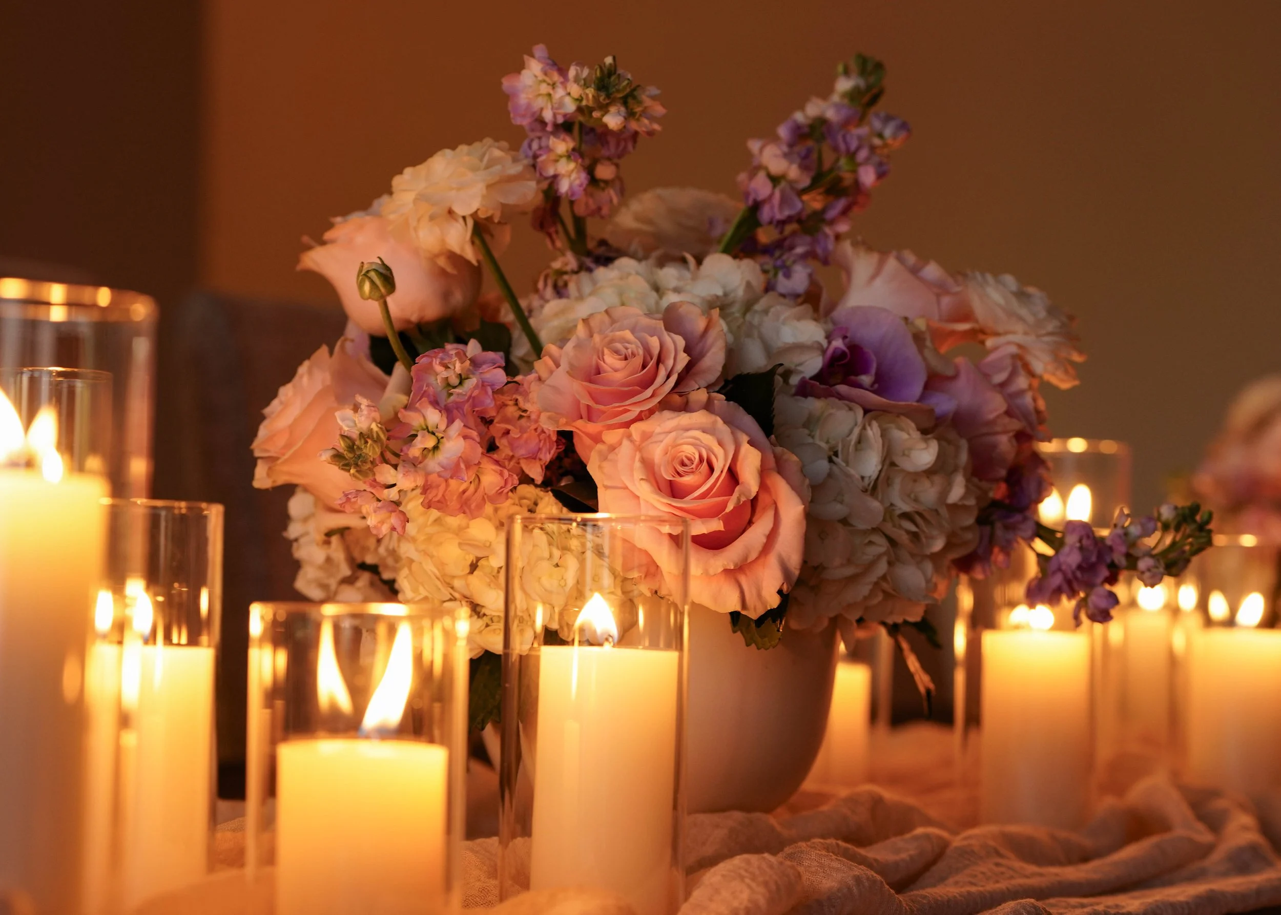 Photo by Black Light Imaging - Close up of a floral arrangement and lit candles on a table.
