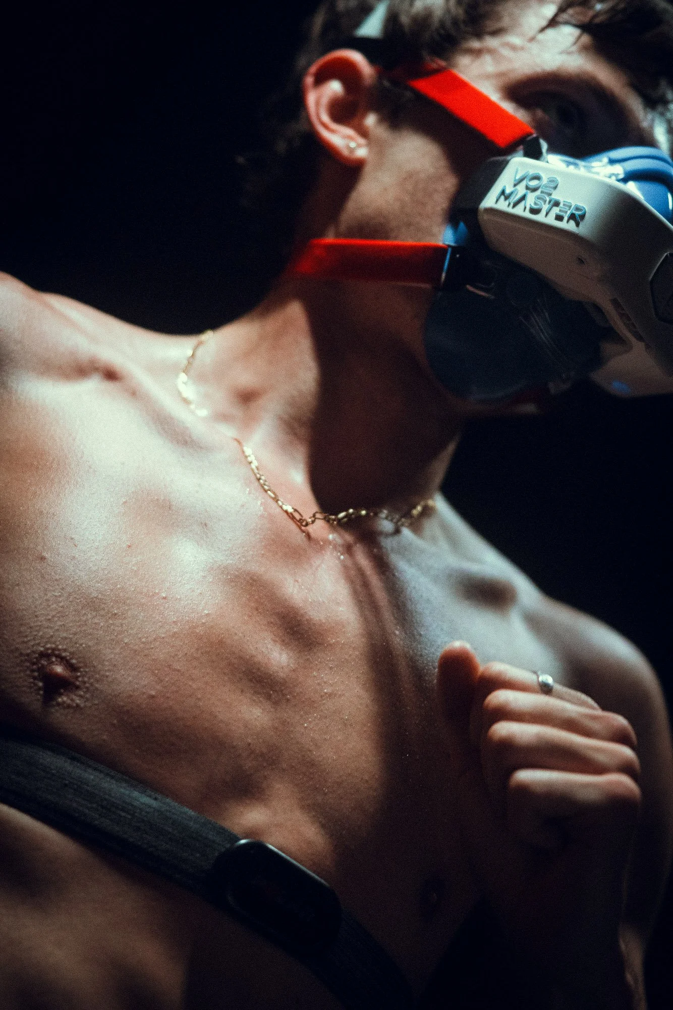 A shirtless person with a necklace, wearing a VR headset labeled 'V2 MASTER', and their eyes are closed with a hand near their chest.
