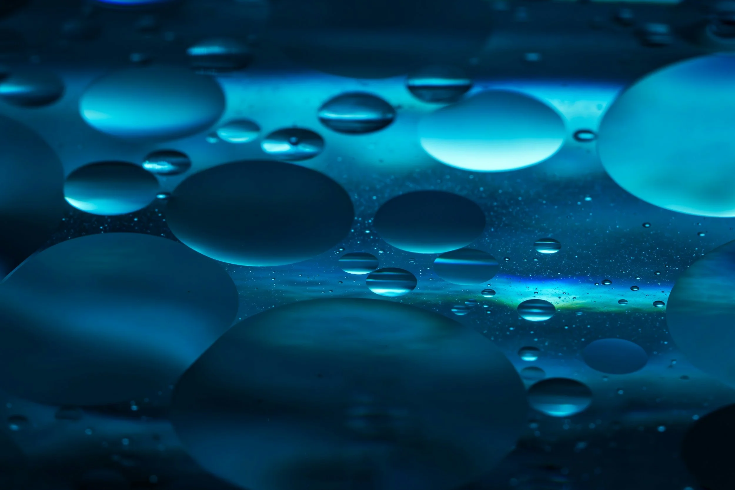 Close-up of oil droplets floating in water, illuminated with blue light.