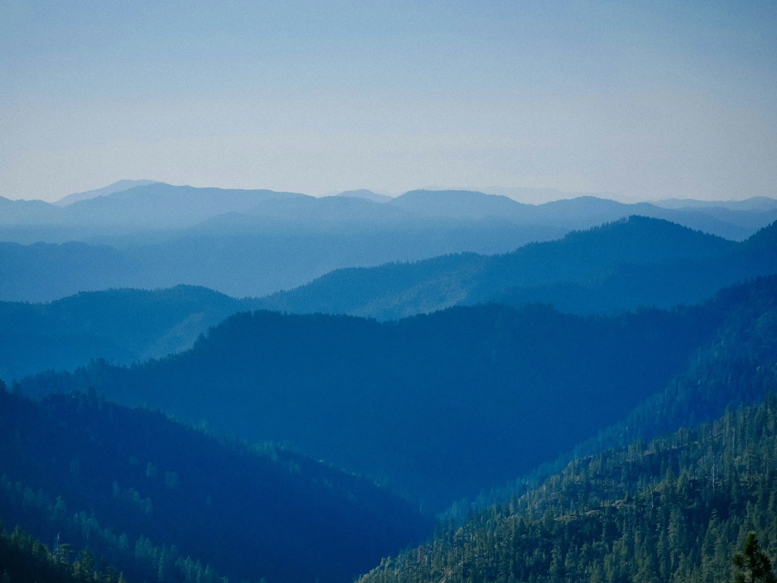 Multiple layers of blue mountain ranges under a clear sky, creating a scenic view of distant hills.