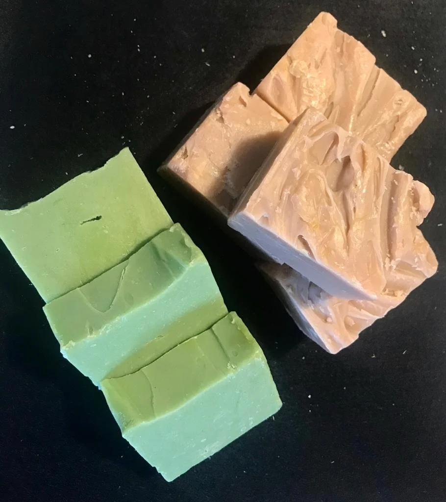 Seis barras de sabonete, três verdes e três bege, organizadas sobre uma superfície preta.