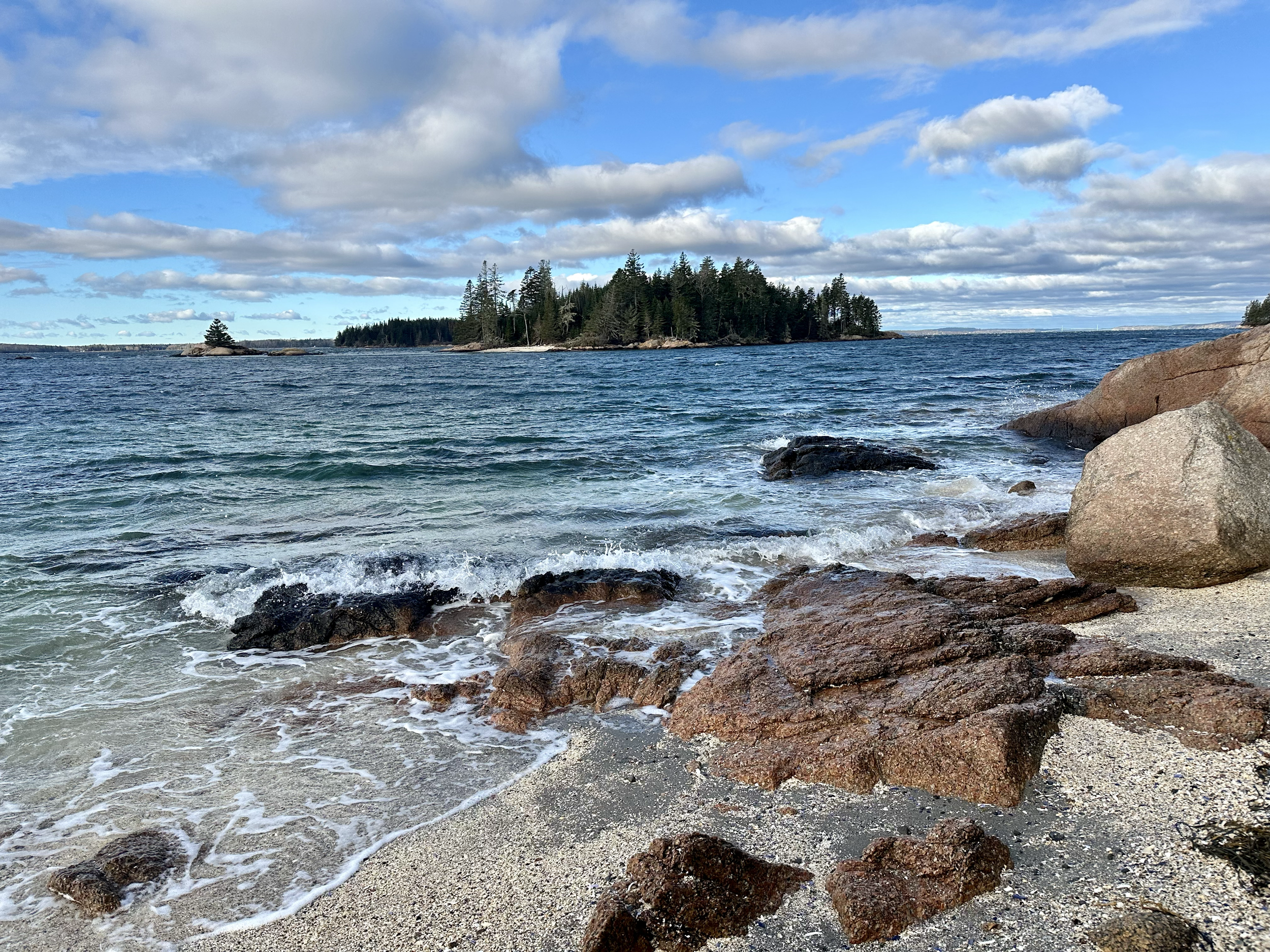 High Head Maine Brooklin Maine- A rocky shoreline with water in the foreground, an island covered with trees in the middle distance, and a cloudy sky above.