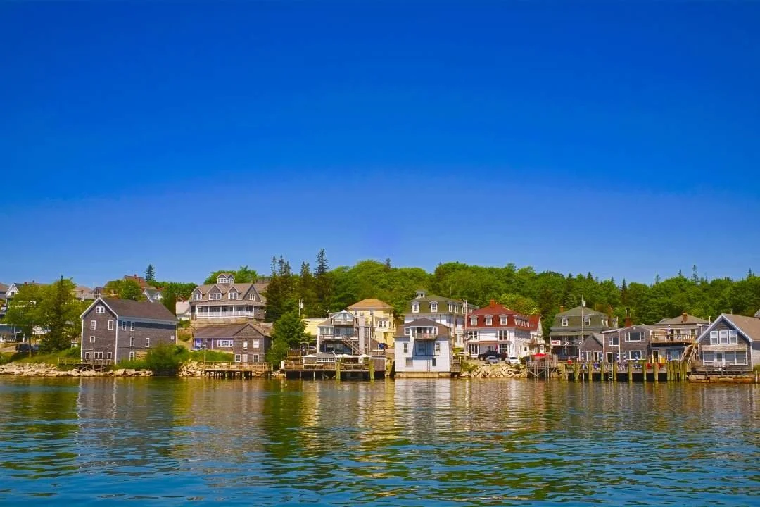 A waterfront view of colorful houses and cottages along a river, with a bright blue sky above.