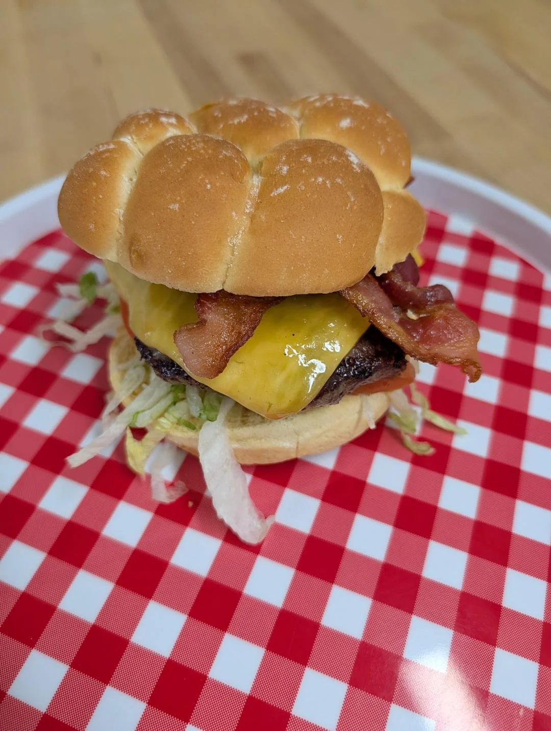 Close-up of a bacon cheeseburger with lettuce, cheese, bacon, and a sandwich bun, placed on a red and white checkered paper on a tray.