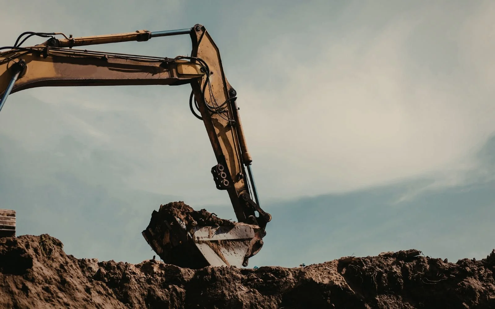 Close-up of an excavator bucket digging into the soil against a cloudy sky.