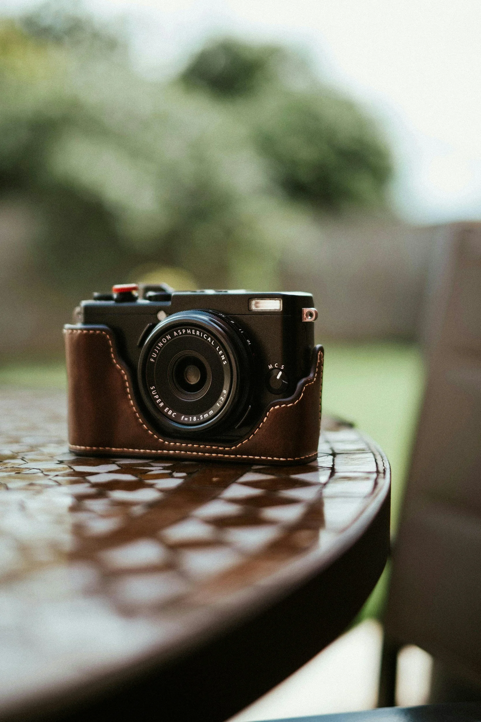 A vintage camera with a leather case on a wooden outdoor table.