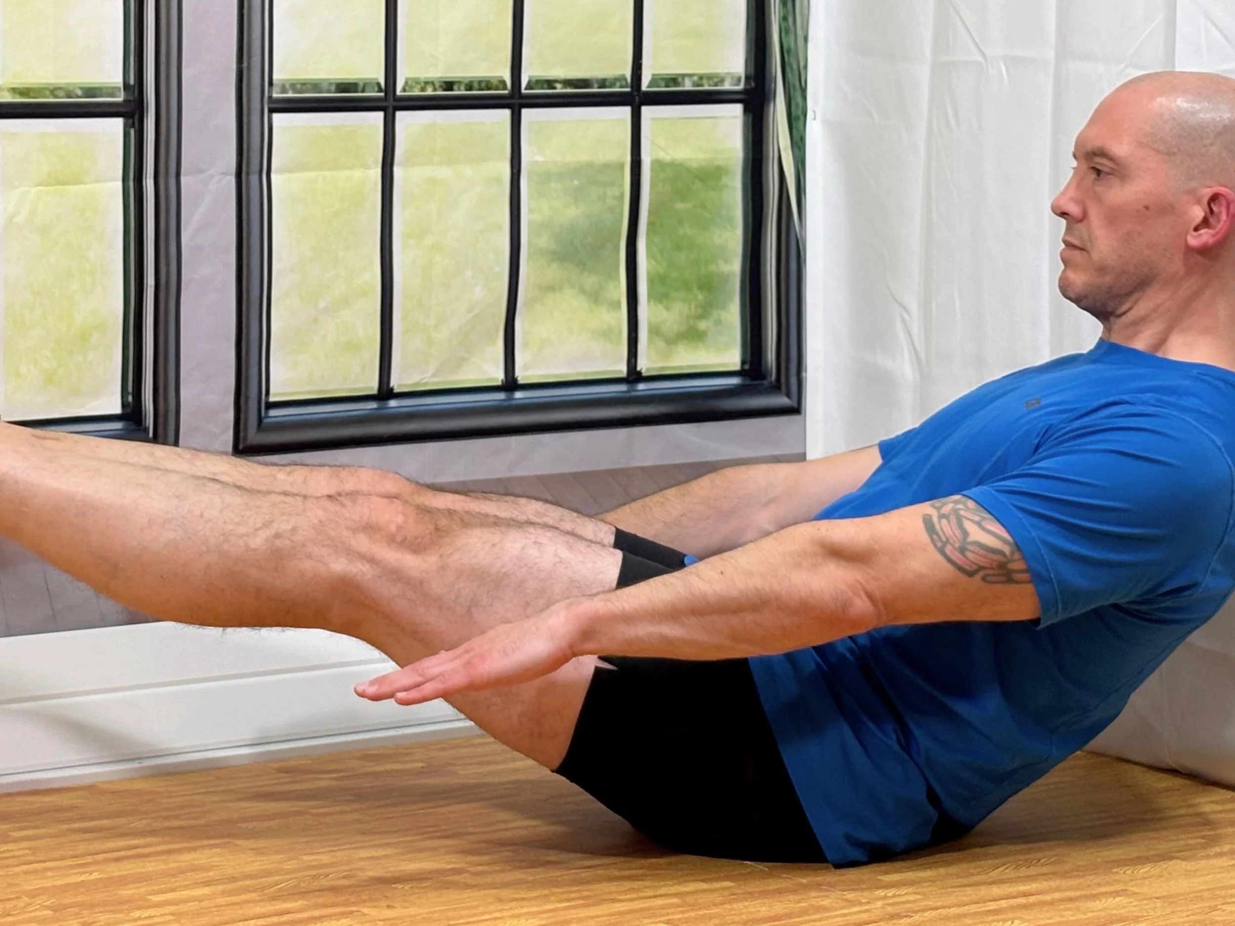 Shane demonstrating a V-sit core exercise during a beginner HIIT Pilates virtual class