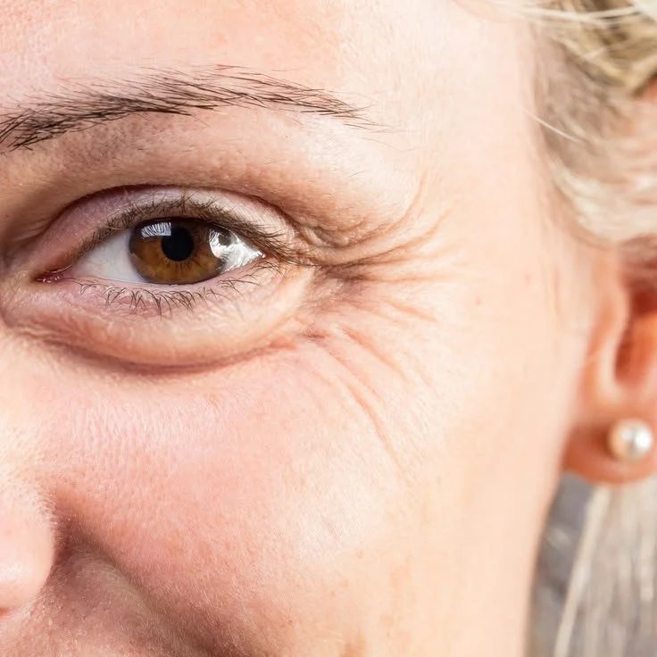 Close-up of a smiling woman's face, showing her eye, cheek, and part of her ear with a pearl earring.