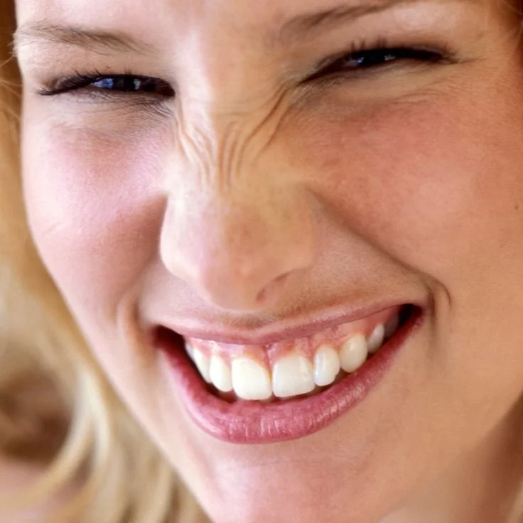 Close-up of a woman smiling with eyes closed, showing her teeth and facial wrinkles from laughing.
