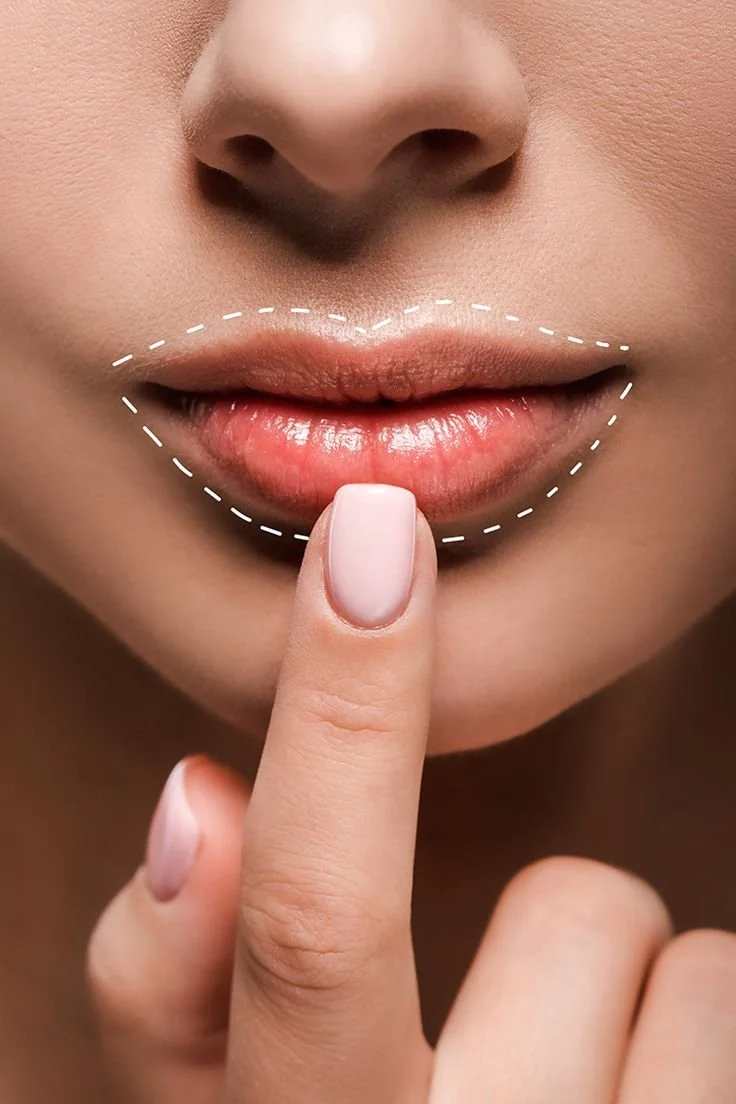 Close-up of a woman with her finger pressed against her lips, which are outlined with a dashed line for lip enhancement or makeup application.