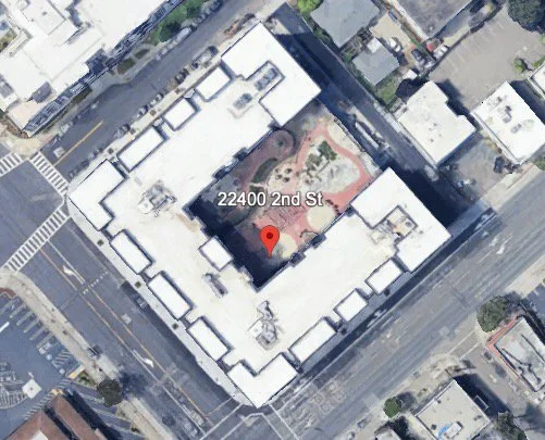 Aerial view of a large white building with a courtyard, located at 22400 2nd St, with surrounding streets and adjacent buildings.