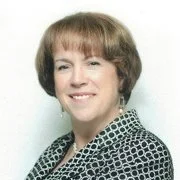 A woman with short brown hair, smiling, wearing a patterned blouse.