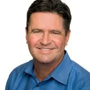 A smiling man with dark hair, wearing a blue shirt, against a plain white background.