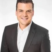 Portrait of a smiling young man in a gray suit and white shirt against a white background.