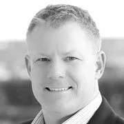 Black and white photo of a smiling man with short hair wearing a suit and tie.
