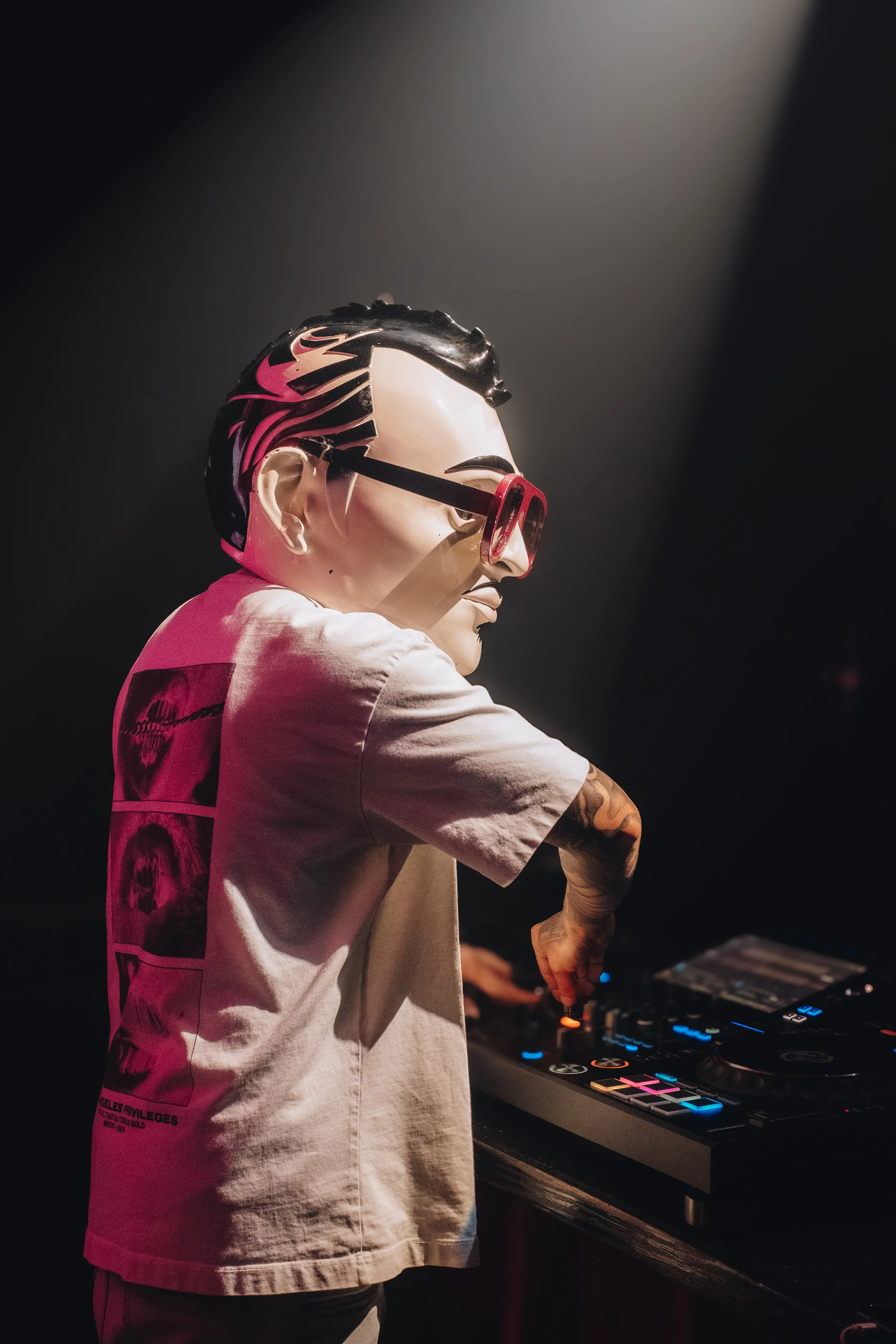 Person in a mask and sunglasses DJing at a turntable with a dark background.