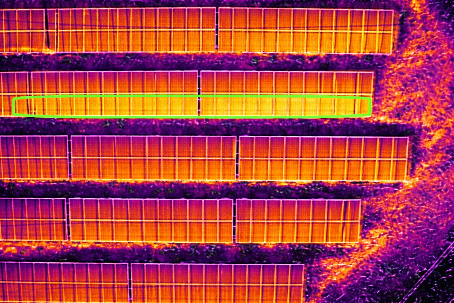 Aerial view of solar panels in a field with one panel highlighted in yellow and green.