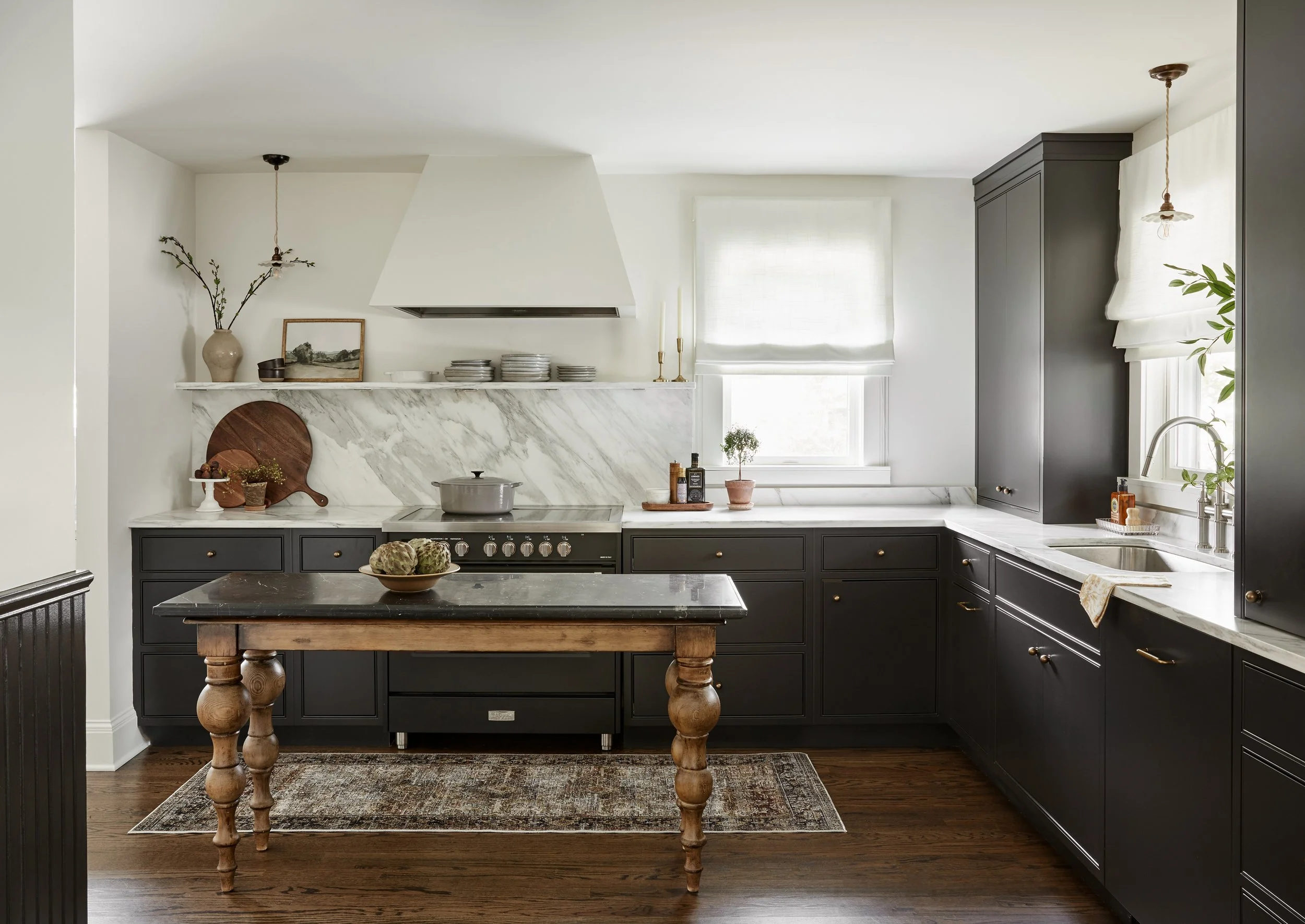 Modern kitchen with dark cabinets, white marble countertops, a marble backsplash, a small island with a wooden top, and a window with white blinds