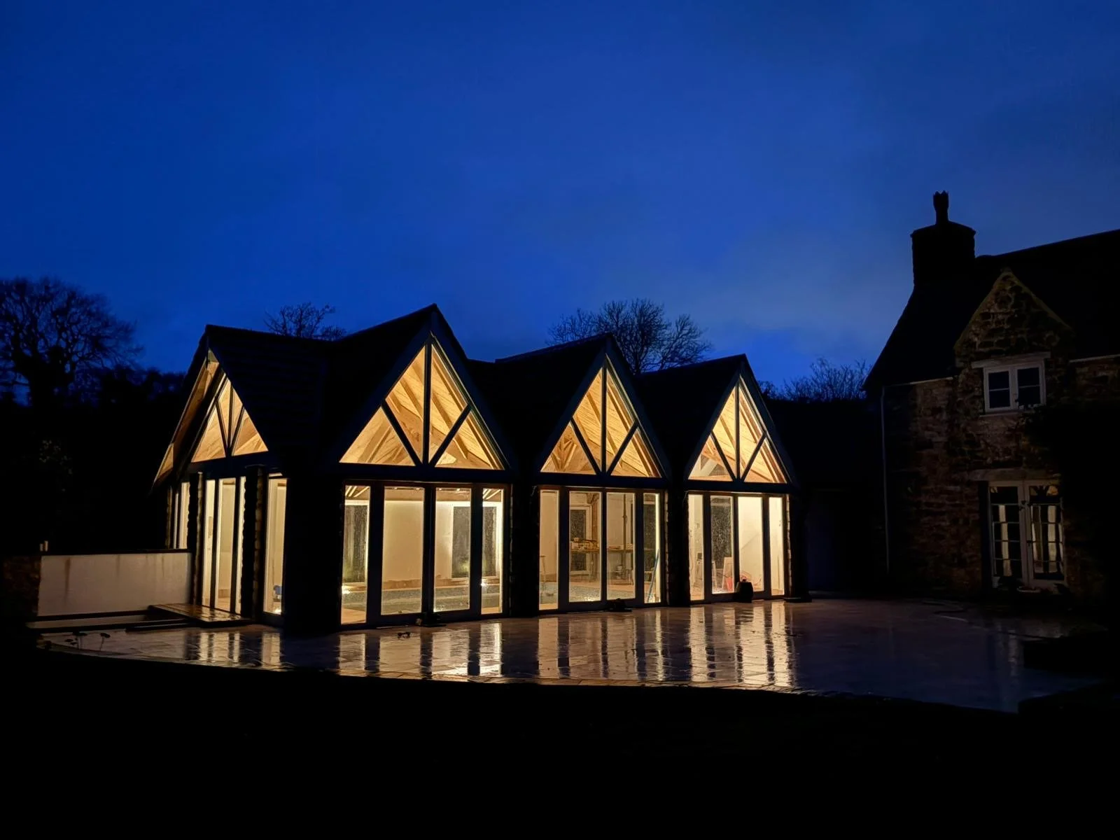 Modern glass extension with pitched roof illuminated within, for a  traditional stone house