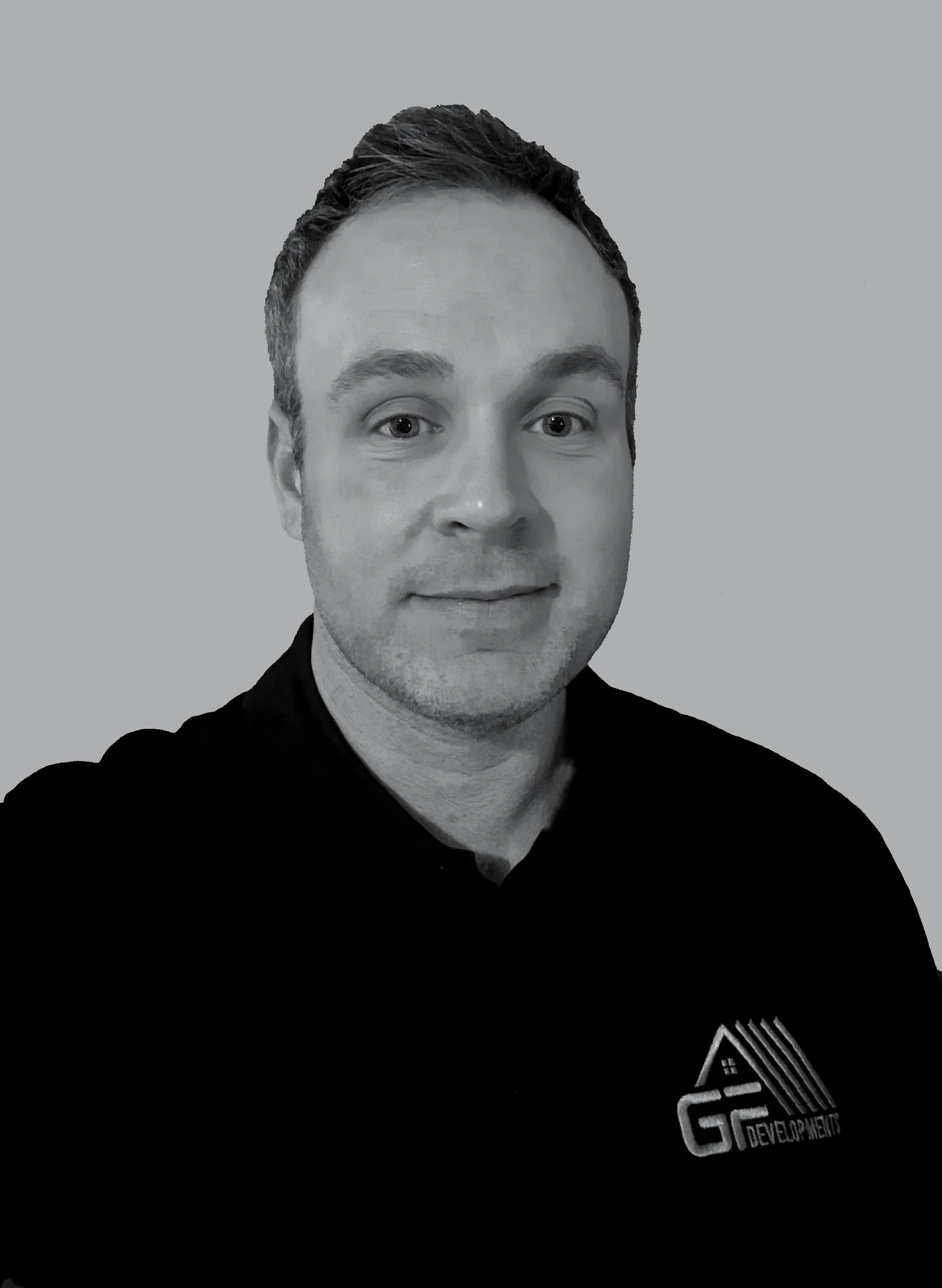 Black and white portrait of a man with short, dark hair, wearing a black polo shirt with a logo on the left side that reads 'G F Developments'.