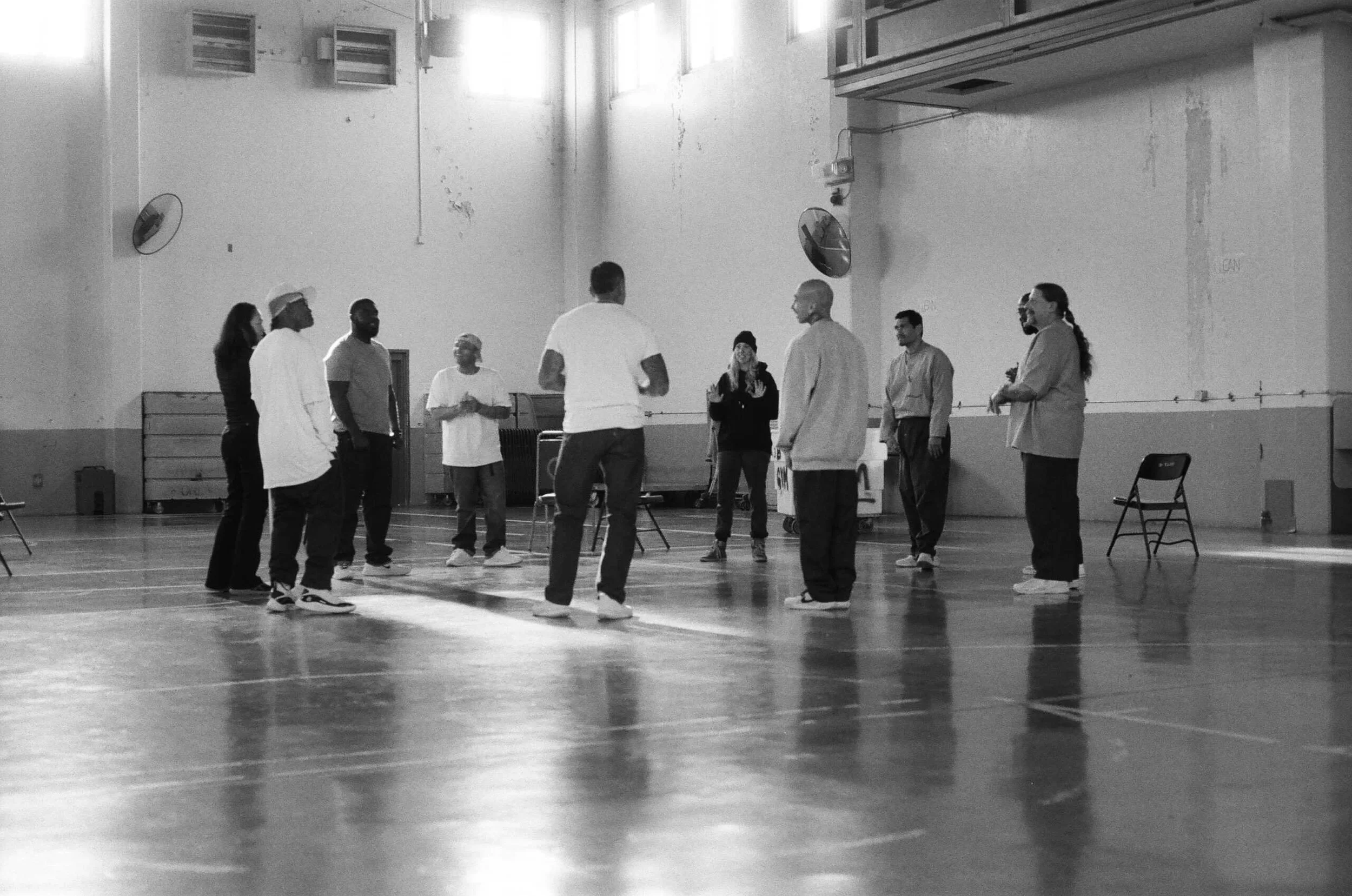 A circle of men in prison uniforms raising their arms up to the sky.