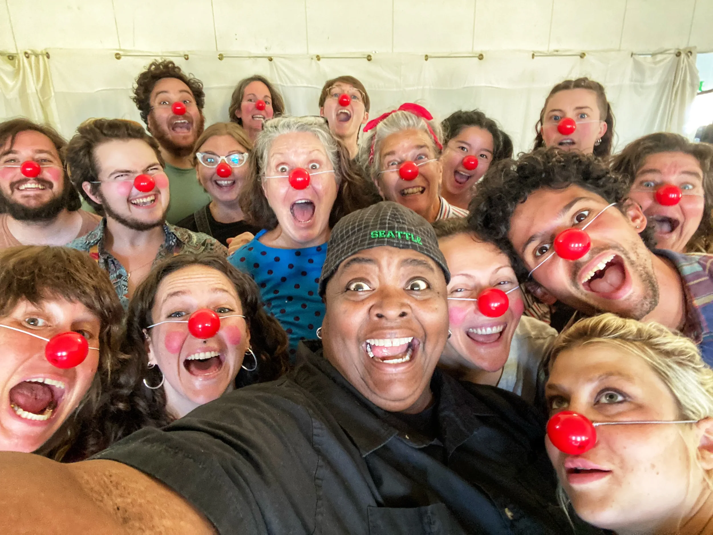 A group of people wearing red clown noses and smiling for a group selfie, with some showing excited and happy expressions.