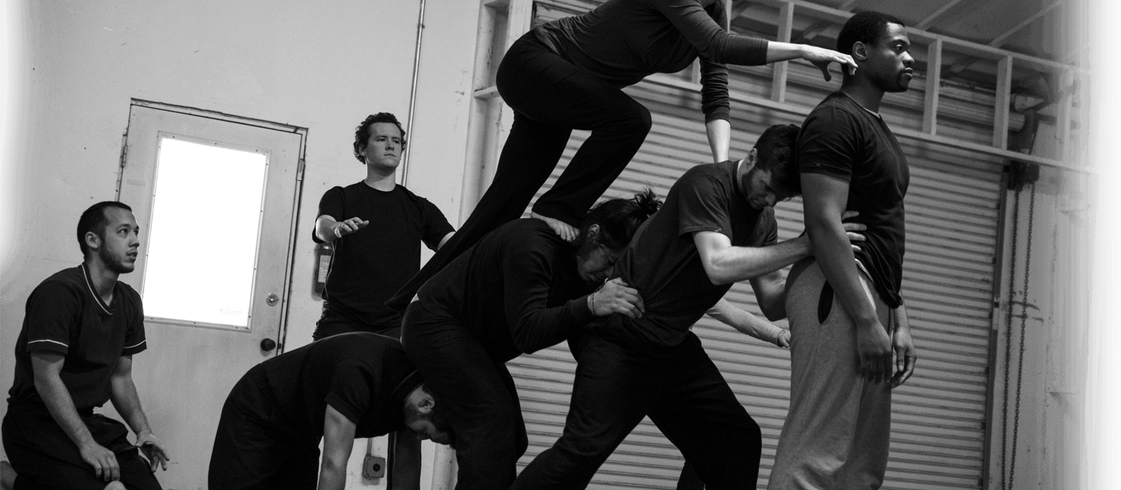 Group of people performing a human tower formation during a practice or performance in an indoor gym or studio.