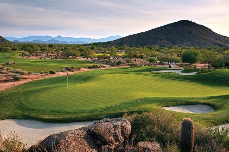 Golf green with bunkers, boulders and a saguaro below a desert mountain in the Scottsdale area