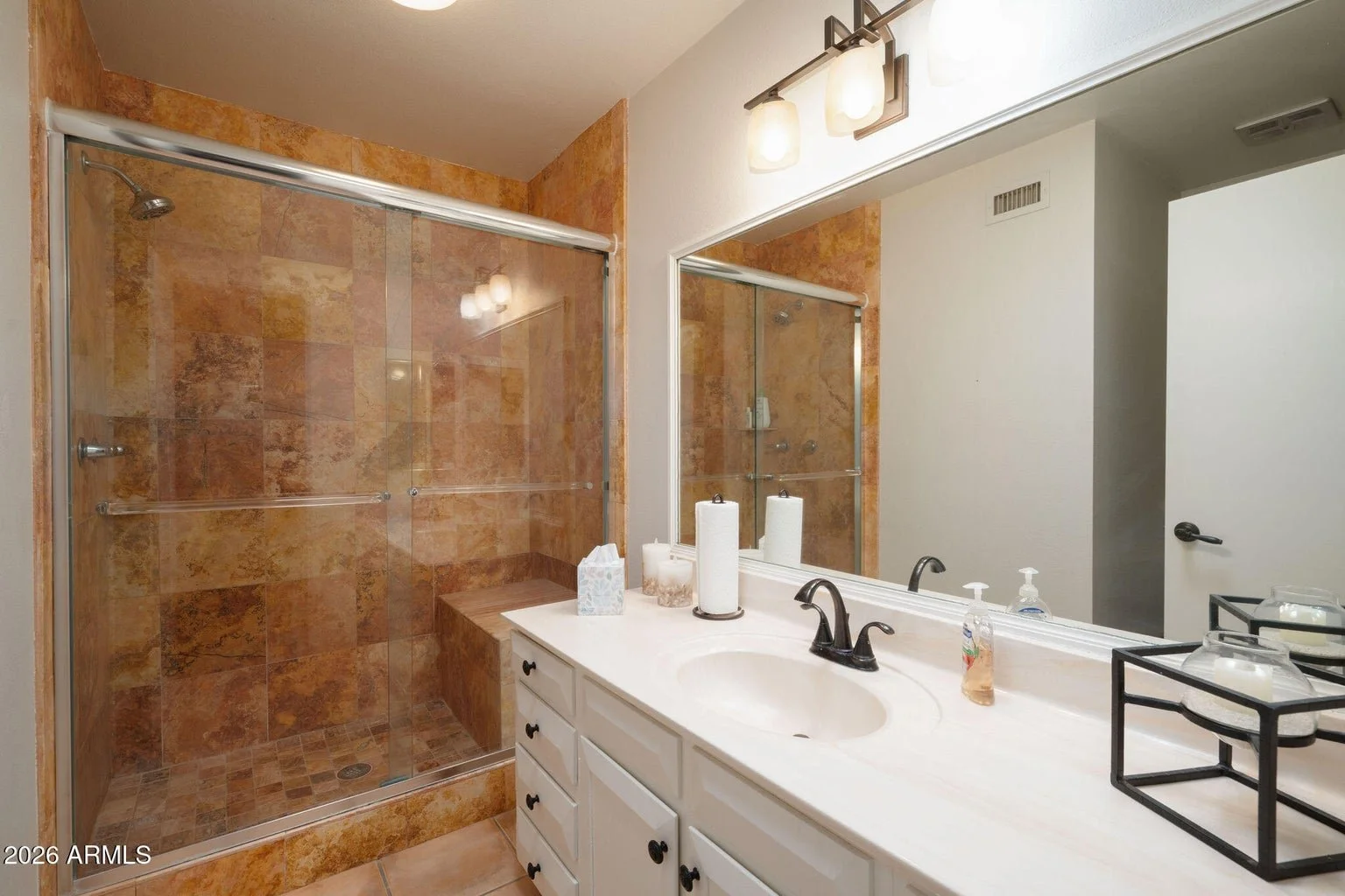 Bathroom at 7401 N Scottsdale Rd #26 in The Shores at McCormick Ranch, Scottsdale, featuring a glass-enclosed walk-in shower with stone-look tile, built-in shower bench, white vanity, and large mirror.