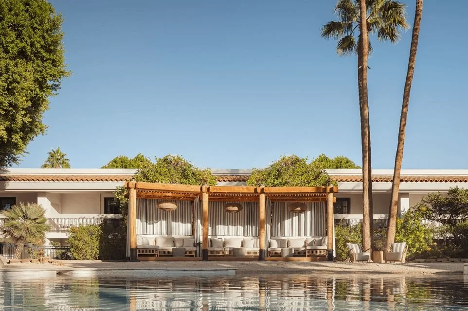 Luxury pool with private cabanas at The Scott Resort & Spa in Scottsdale, Arizona, surrounded by palm trees and lush desert landscaping.