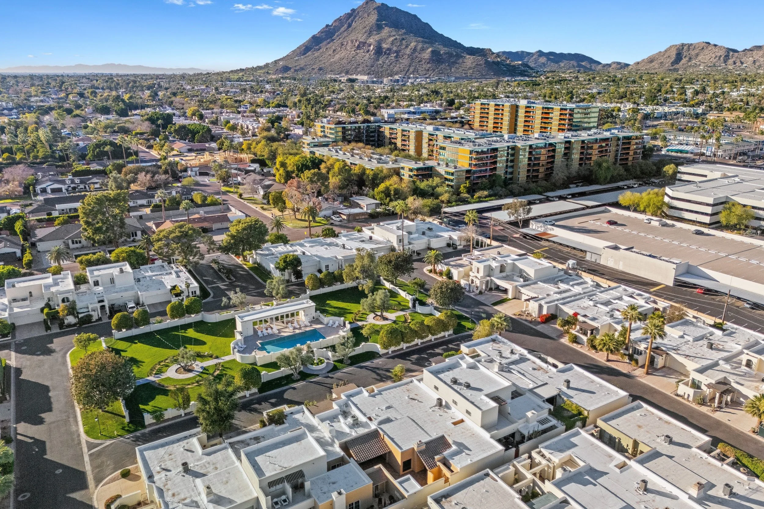 Aerial view of a neighborhood with white houses, a swimming pool, and a high-rise apartment complex with a mountain in the background.