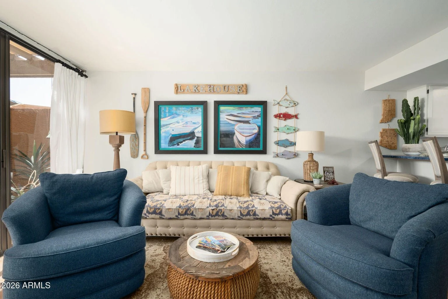 Living area at 7401 N Scottsdale Rd #26 in The Shores at McCormick Ranch, featuring blue upholstered chairs, a cream sofa, lake-inspired wall art, and natural light from patio doors.