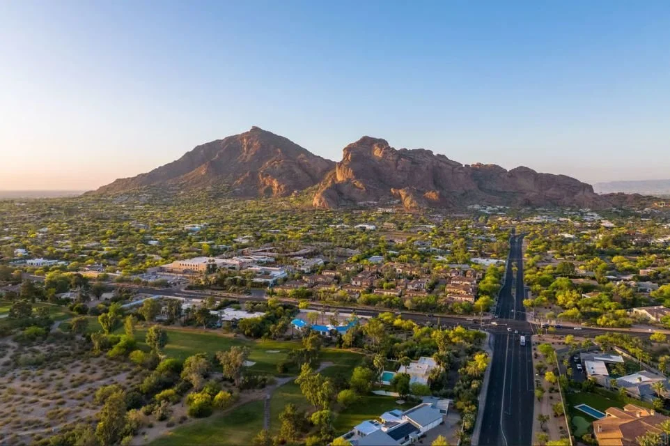 Aerial view of Arcadia Phoenix with Camelback Mountain at sunset, showcasing tree-lined neighborhoods, luxury homes, golf course, and scenic desert landscape
