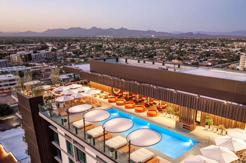 Rooftop pool at The REMI, Autograph Collection in Scottsdale, overlooking the city skyline with luxury cabanas and mountain views at dusk.