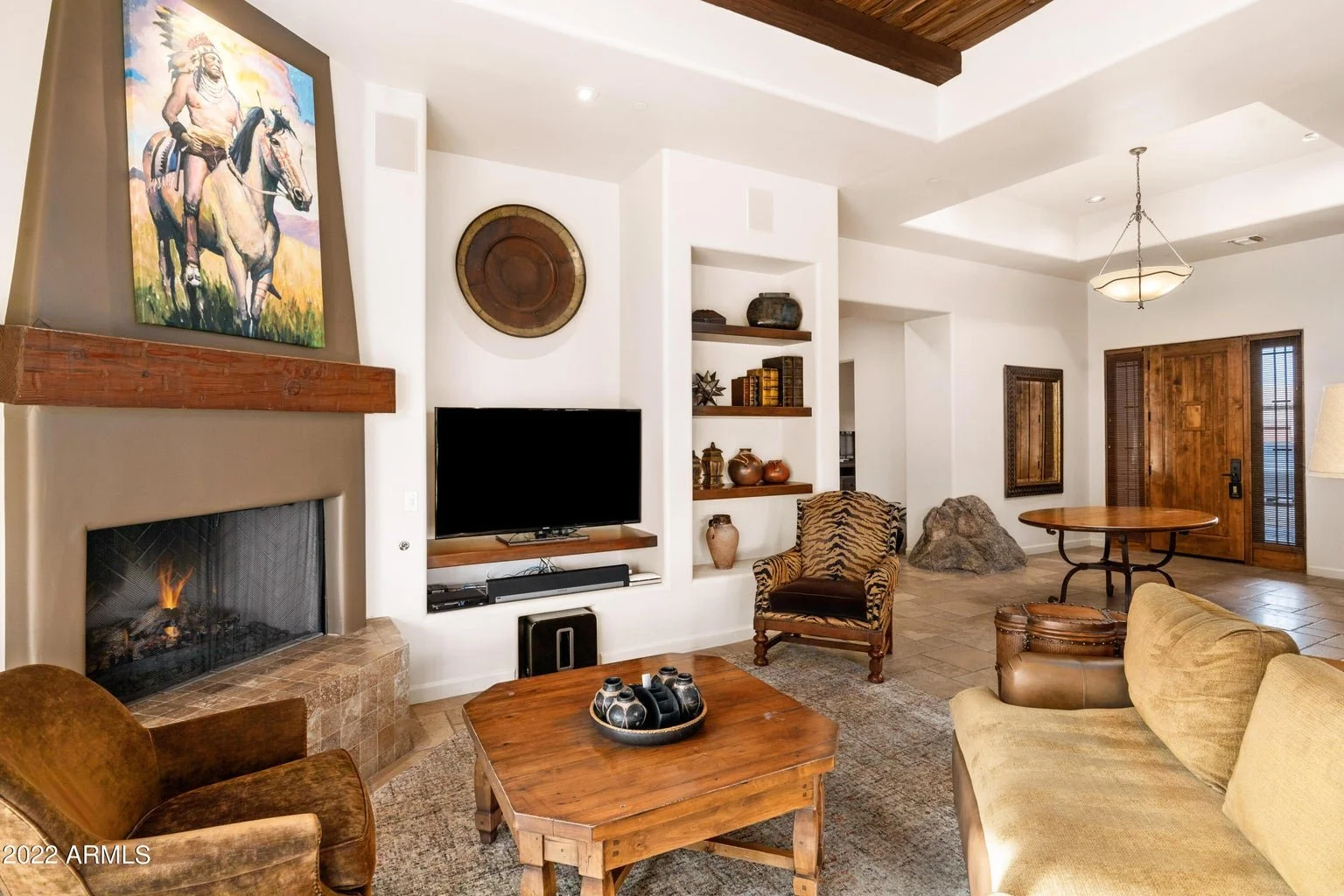 Rustic luxury living room in Scottsdale, Arizona, featuring a fireplace with wood mantel, built-in shelving, natural stone flooring, and a wooden front entry door.