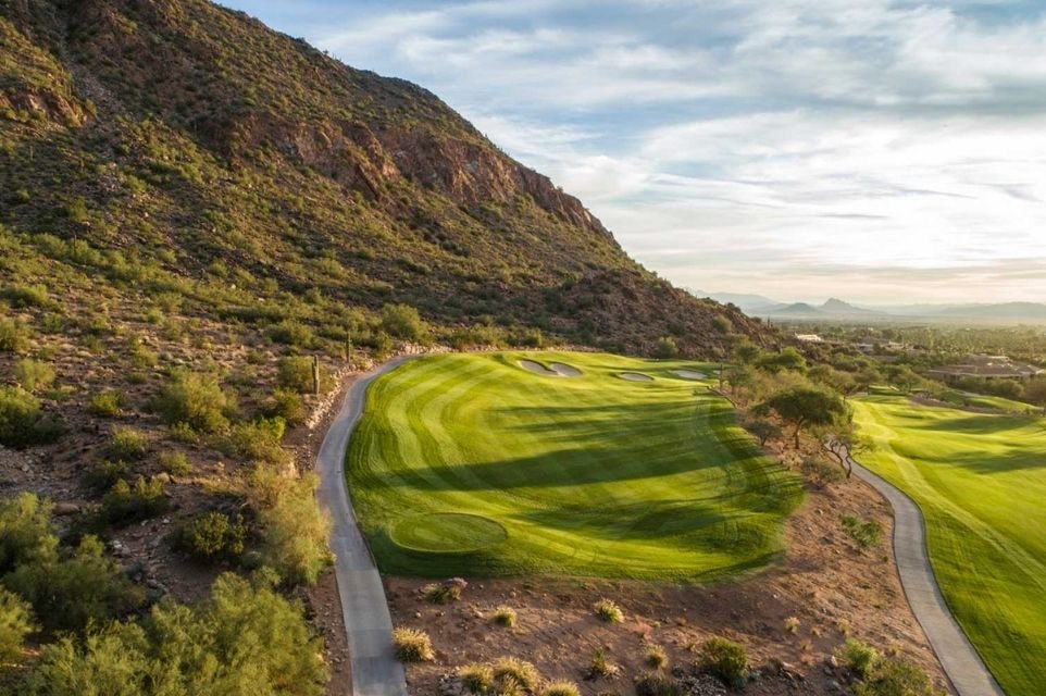 Desert golf fairway winding below a rugged mountainside with cart paths near Scottsdale, Arizona