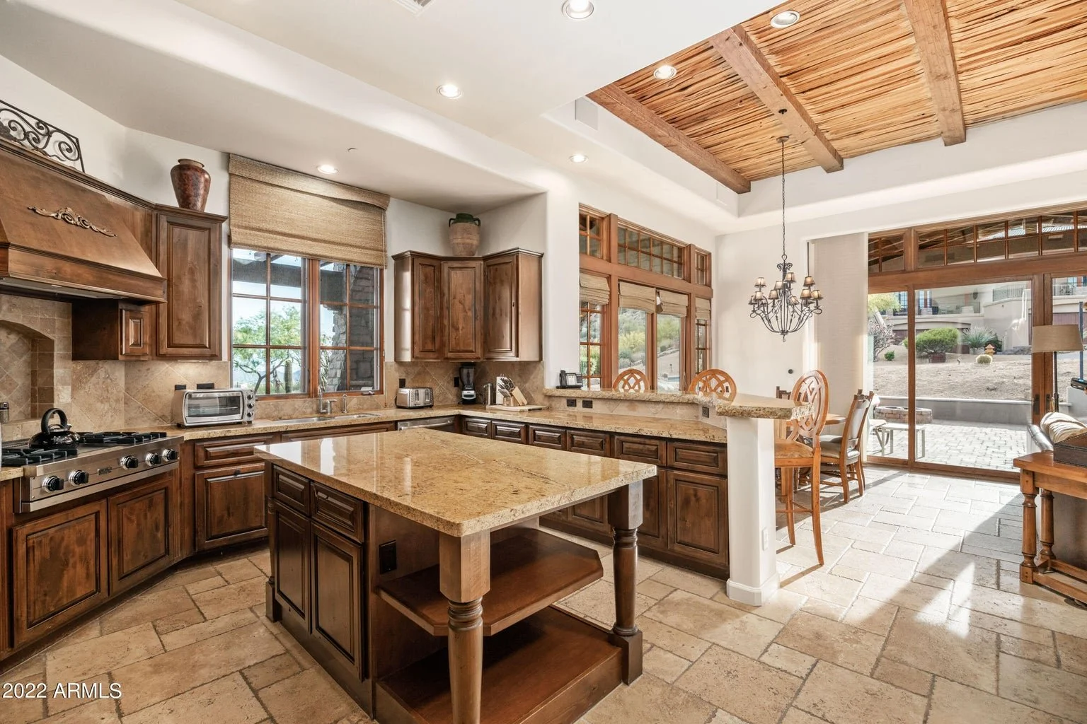 Kitchen with wooden cabinets, granite countertops, and a central island. Includes a stove, toaster, coffee maker, and large windows showing an outdoor patio.