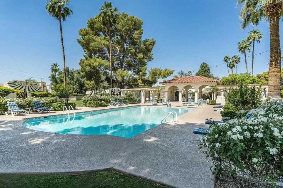 Resort-style community pool at Villa d’Este in Scottsdale Arizona featuring lush landscaping, palm trees, shaded lounge areas, and luxury townhome amenities.