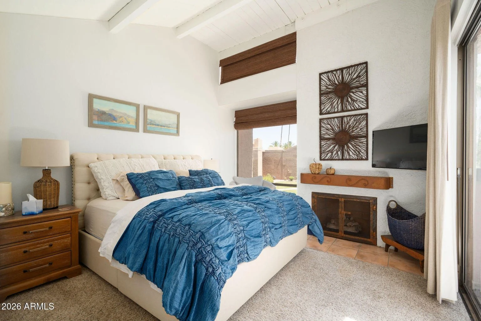 Spacious bedroom at 7401 N Scottsdale Rd #26 in McCormick Ranch, Scottsdale, featuring a vaulted ceiling, fireplace, blue bedding, and large windows overlooking the landscaped community.