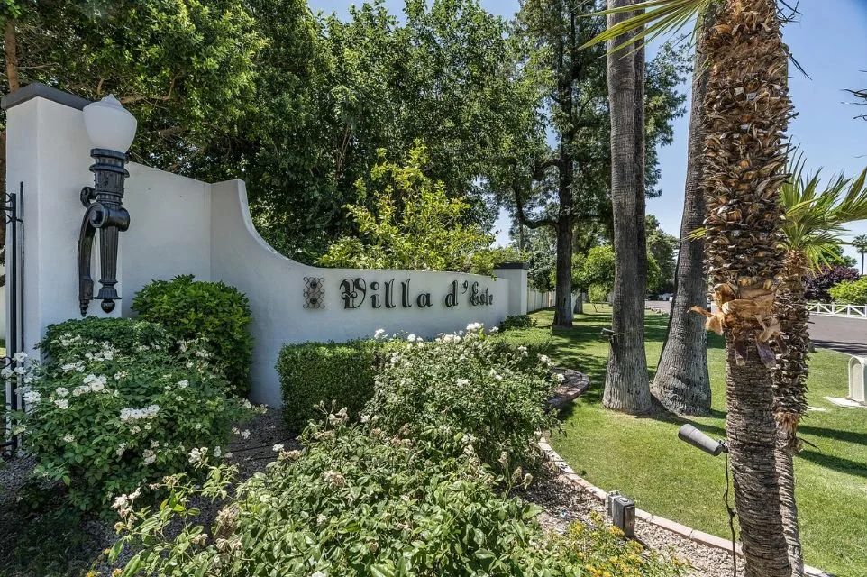 Villa d’Este Scottsdale community entrance with landscaped greenery, palm trees, and Mediterranean-style signage in a quiet residential neighborhood