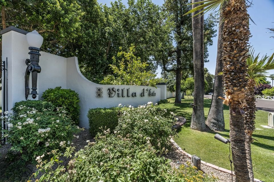 Villa d’Este entrance monument sign surrounded by mature landscaping and palm trees in a luxury Scottsdale townhome community.